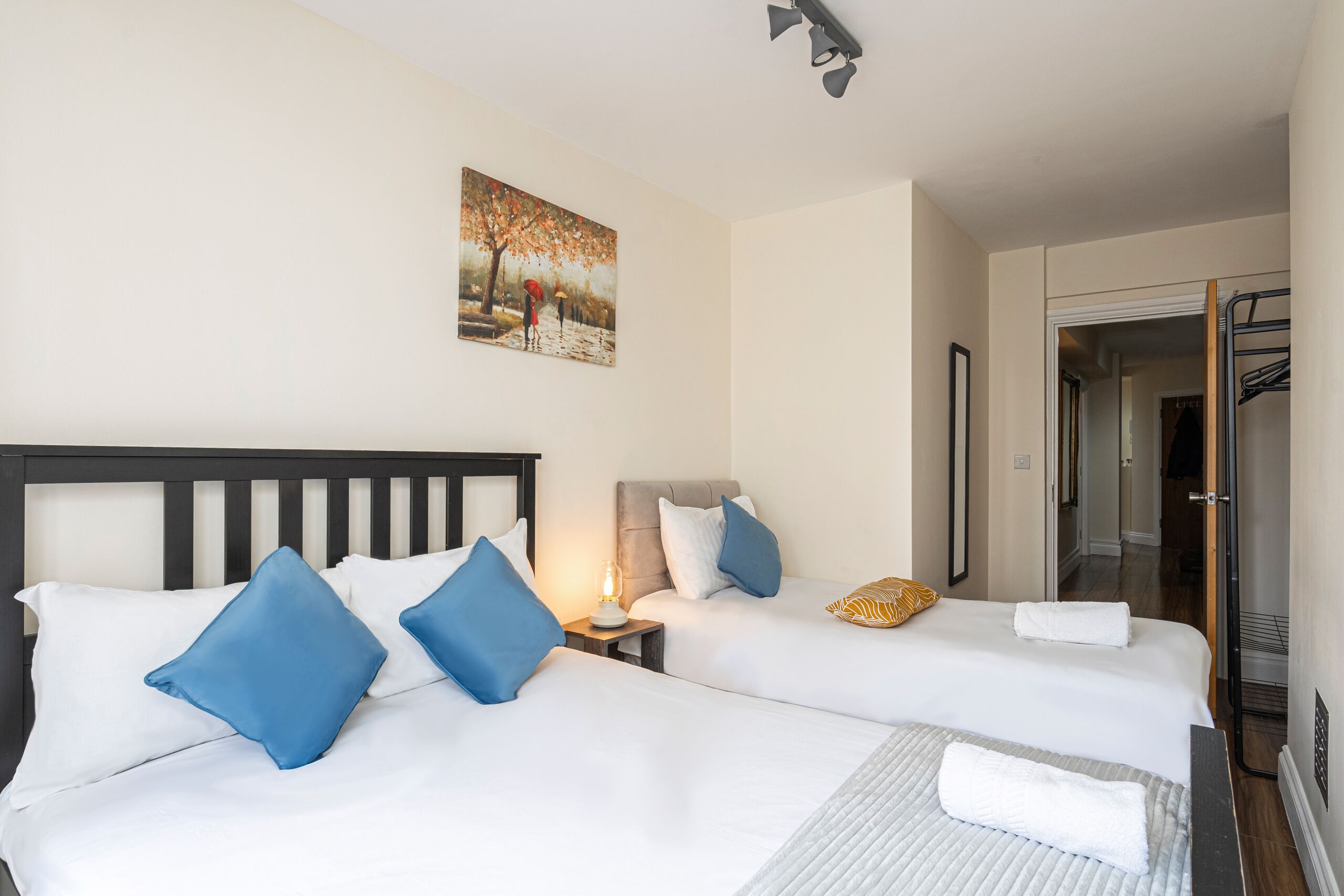 A hotel room with two beds, a painting on the wall, and a door leading to a bathroom.