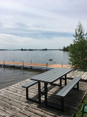 En träbrygga med picknickbord med utsikt över en lugn sjö.