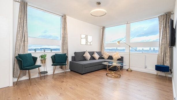 A modern living room with a grey sofa, two green armchairs, a coffee table, and a floor lamp. - Lovely Apartments in Landward Court (London)