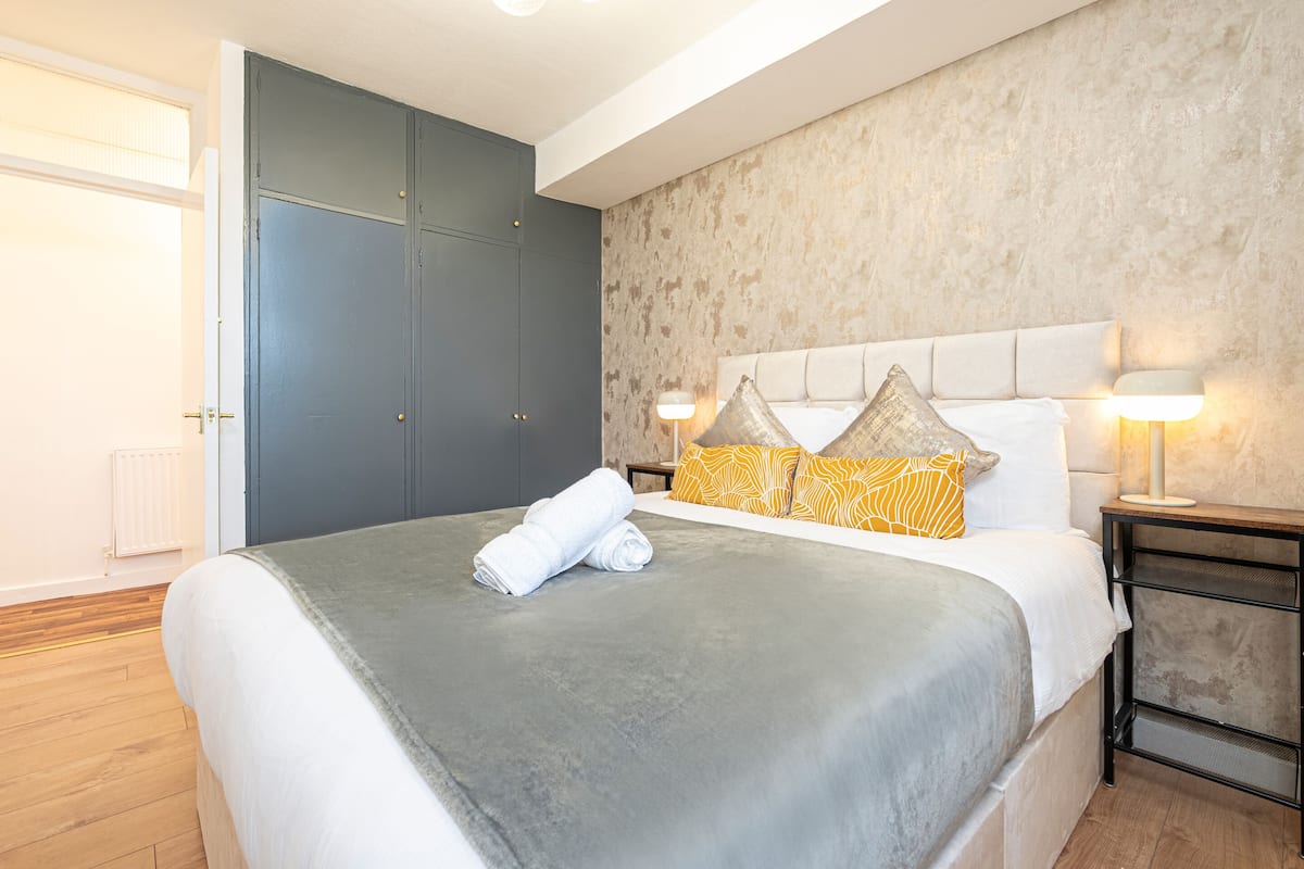 A neatly made bed with a grey blanket, a white headboard, and two bedside lamps.