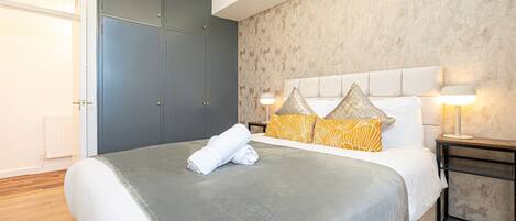 A bedroom with a bed, a nightstand, a lamp, a wardrobe, and a radiator.