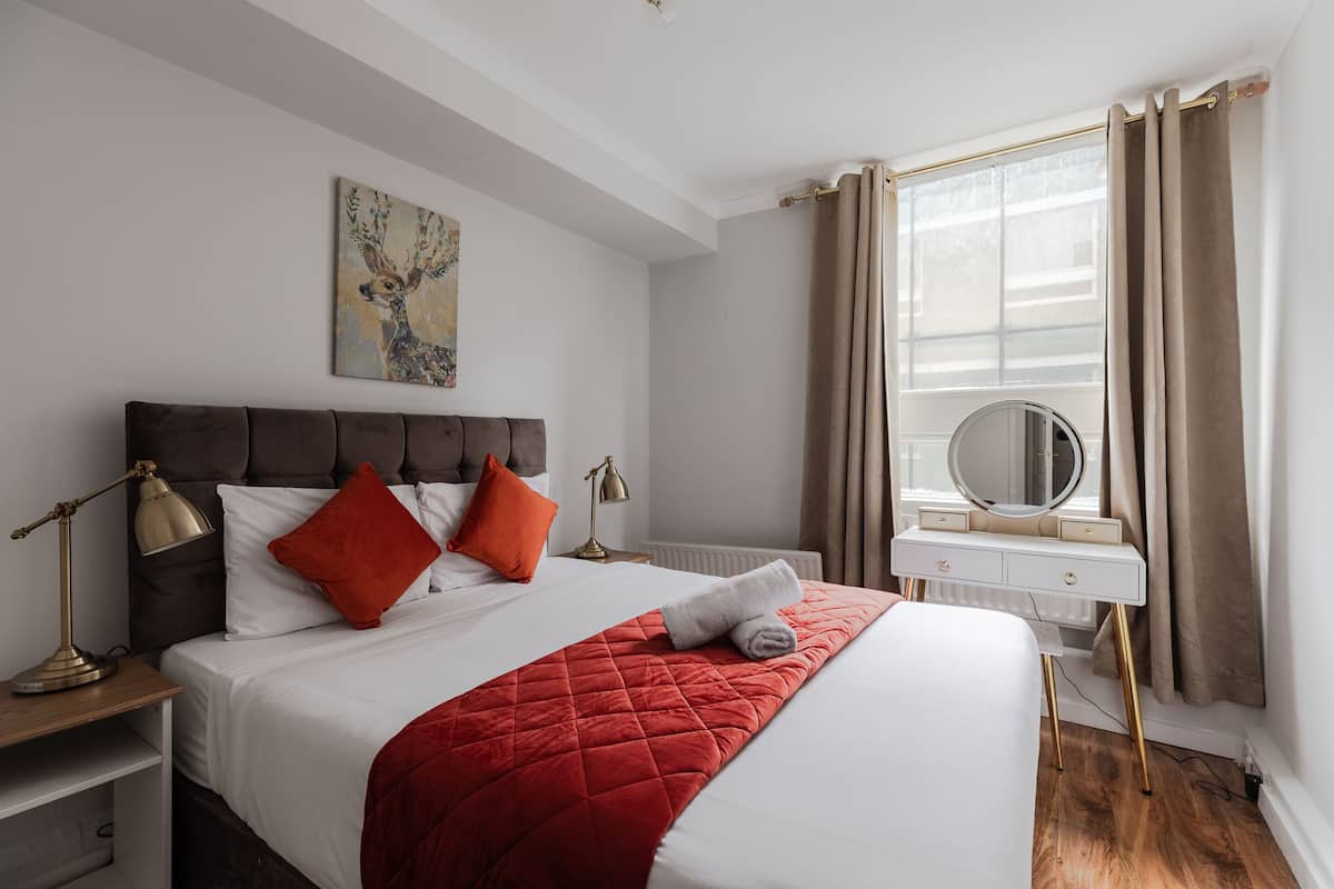 A neatly made bed with a red blanket, a bedside lamp, and a mirror on a dresser.