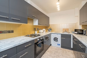 Una cocina moderna con armarios grises, horno empotrado, lavadora y microondas.