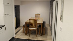 A compact kitchen with white cabinets, a wooden dining table with four chairs, and a small refrigerator. - Ferienhaus Nettes Landhaus (Winterspelt)