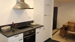 A modern kitchen with white cabinets, a stainless steel range hood, a black countertop, and a dining area with a wooden table and chairs. - Ferienhaus Nettes Landhaus (Winterspelt)