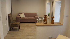 A living room with a sofa, a chair, a small table with a lamp, and a mirror on the wall. - Ferienhaus Nettes Landhaus (Winterspelt)
