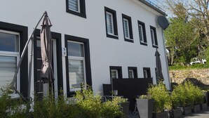 A white building with black window frames and shutters, outdoor seating, and potted plants. - Ferienhaus Nettes Landhaus (Winterspelt)