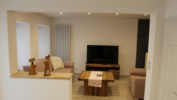 A modern living room with a wooden coffee table, a sofa, a television, and decorative items. - Ferienhaus Nettes Landhaus (Winterspelt)