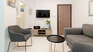 A modern living room with a grey sofa, a grey armchair, a small black table, a TV mounted on the wall, and a wooden door. - Apartment Hermes in Central Athens (Athens)