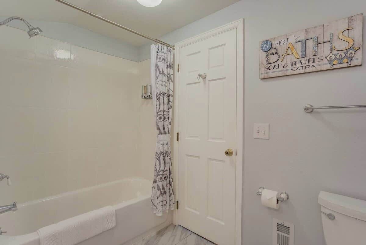 A bathroom with a bathtub, shower curtain, toilet, and a sign on the wall.