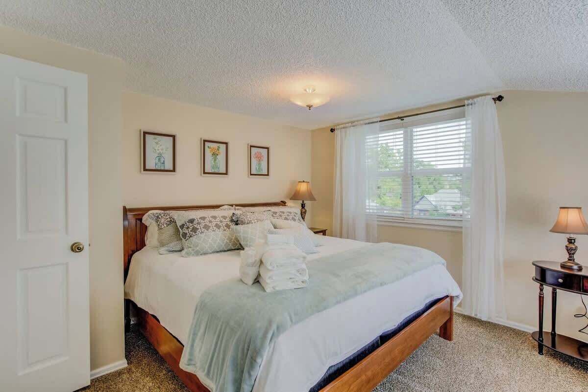 Un dormitorio con cama, mesita de noche, lámpara y ventana con cortinas.