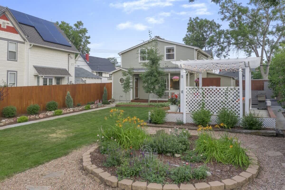 A residential backyard with a garden, a pergola, and solar panels on the house.