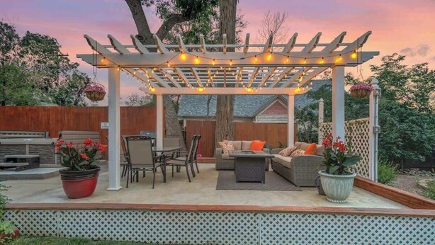Ein überdachter Patio-Bereich mit Gartenmöbeln, einer Pergola mit Lichterketten und Kübelpflanzen.