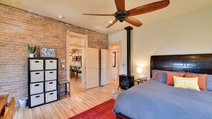 Un dormitorio con cama, ventilador de techo, pared de ladrillo, suelo de madera, alfombra roja y un mueble de almacenaje.