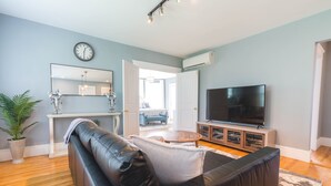 Ein Wohnzimmer mit einer schwarzen Ledersofa, einem Flachbildfernseher, einem großen Spiegel und einer Zimmerpflanze.