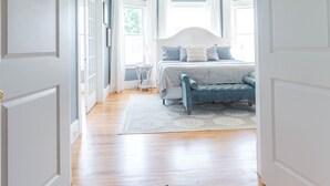 Ein Flur, der zu einem Schlafzimmer mit Bett, Stuhl und Fenster führt.