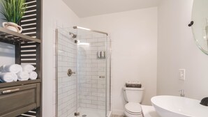 Ein modernes Badezimmer mit einer gläsernen Duschkabine, einer weißen Toilette, einem großen weißen Waschbecken und einem Handtuchhalter mit ordentlich gerollten Handtüchern.