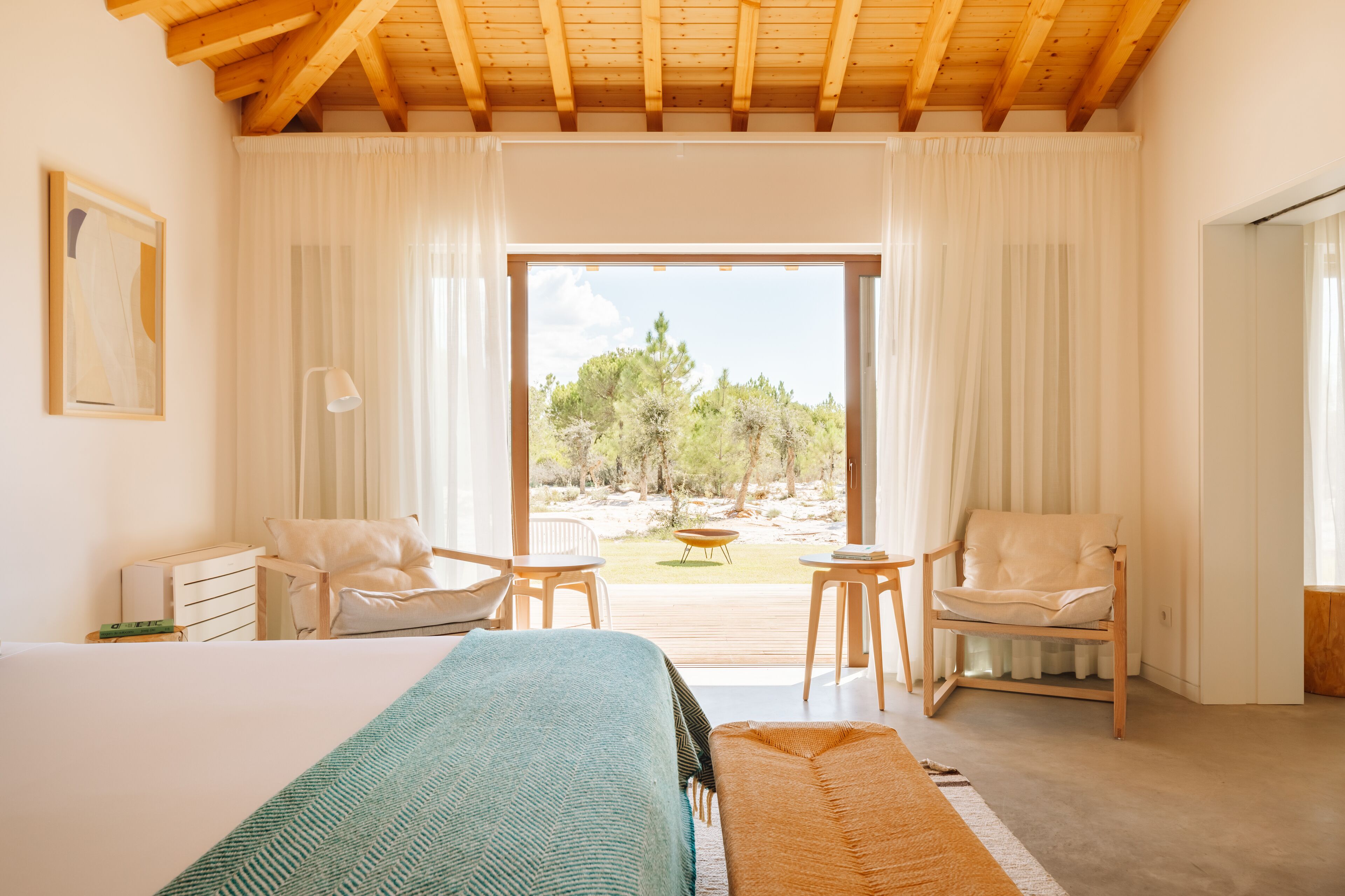 A bedroom with a large bed, two chairs, a small table, and a view of the outdoors.