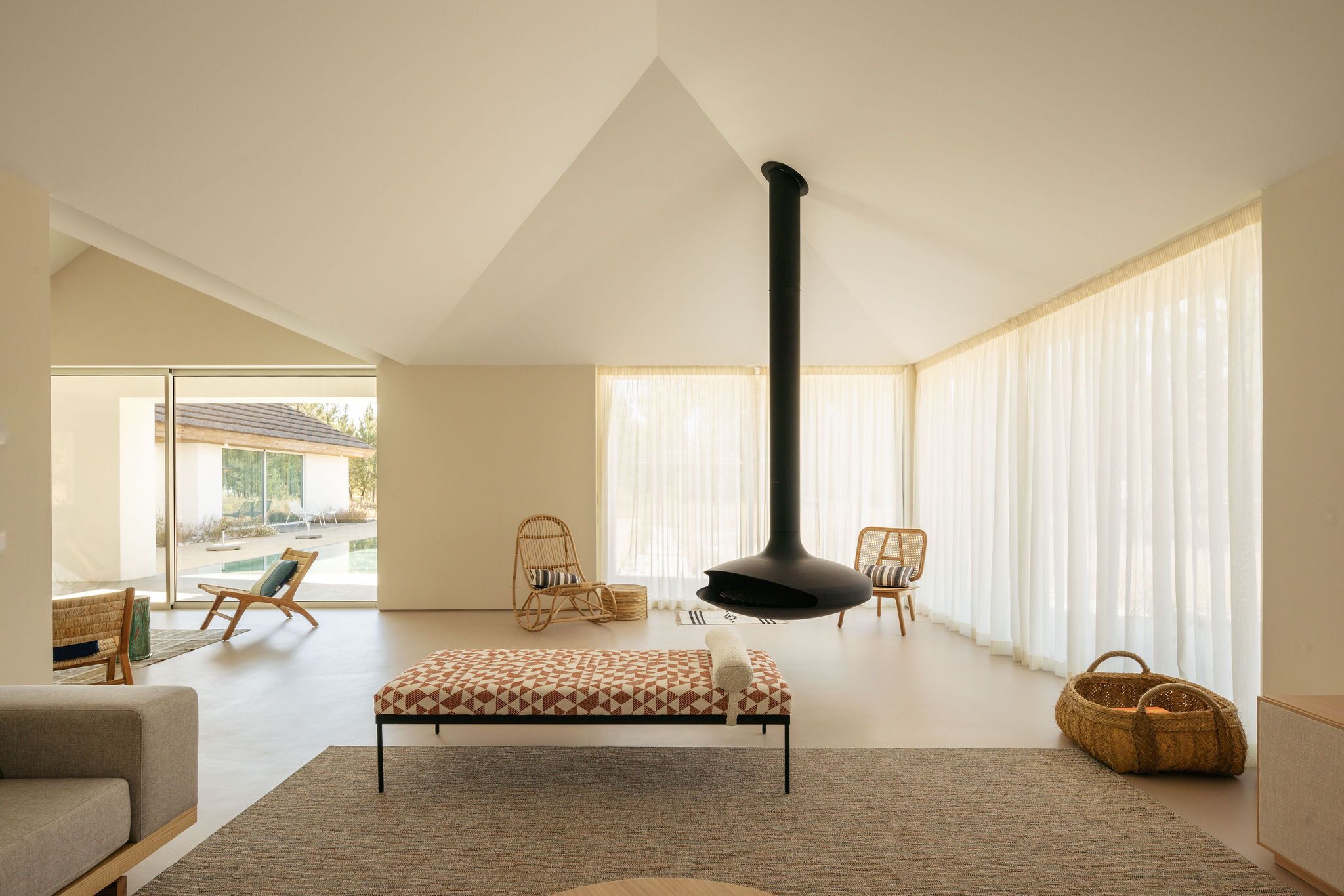 A spacious living room with a high ceiling, a large black fireplace, and a view of a swimming pool outside.