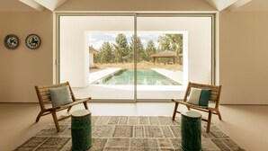 Una habitación con un amplio ventanal corredera que da a una zona de piscina exterior, dos sillas de madera con cojines y una alfombra estampada.