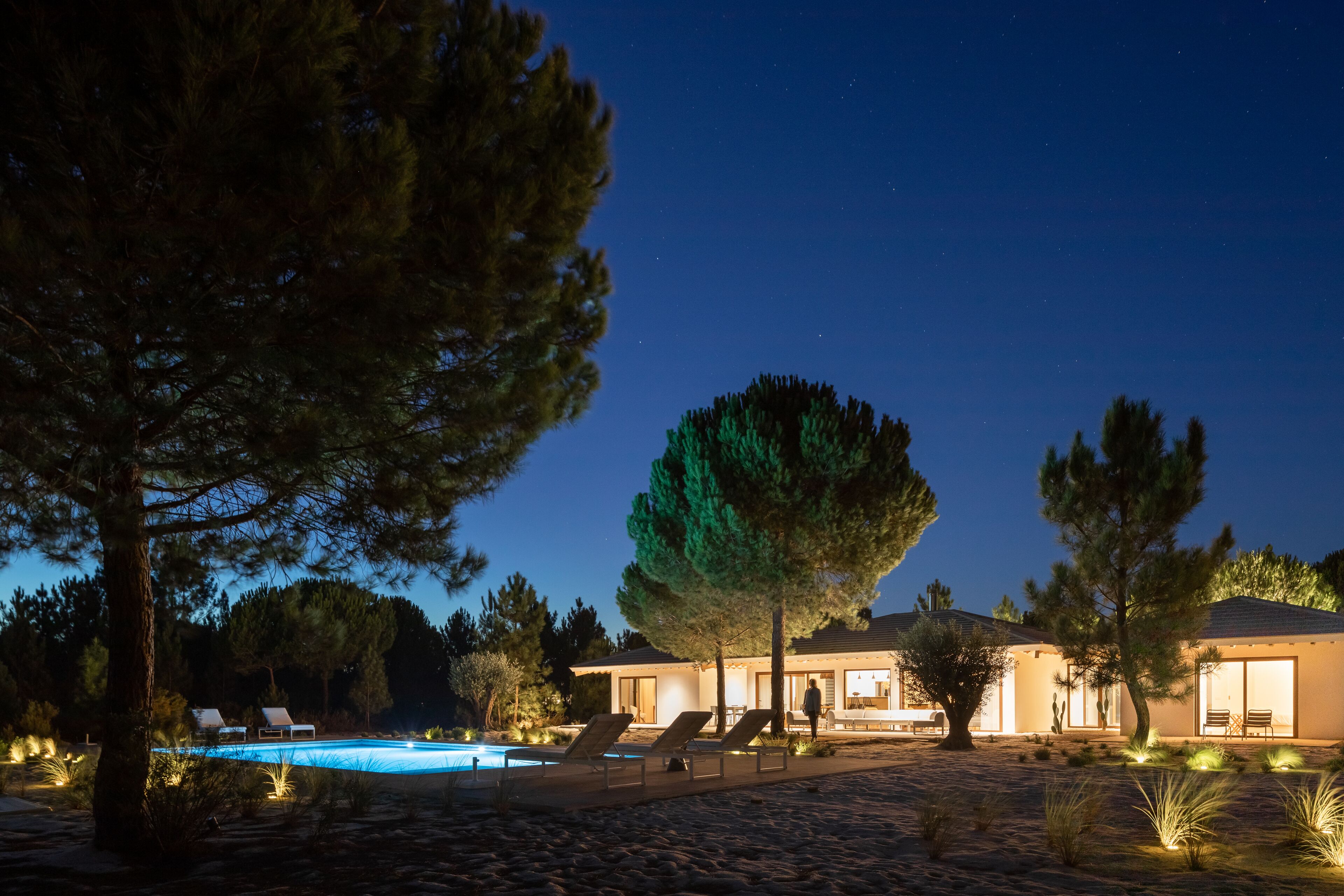 Ein Resort bei Nacht mit Schwimmbad, Liegestühlen und einem gut beleuchteten Gebäude.