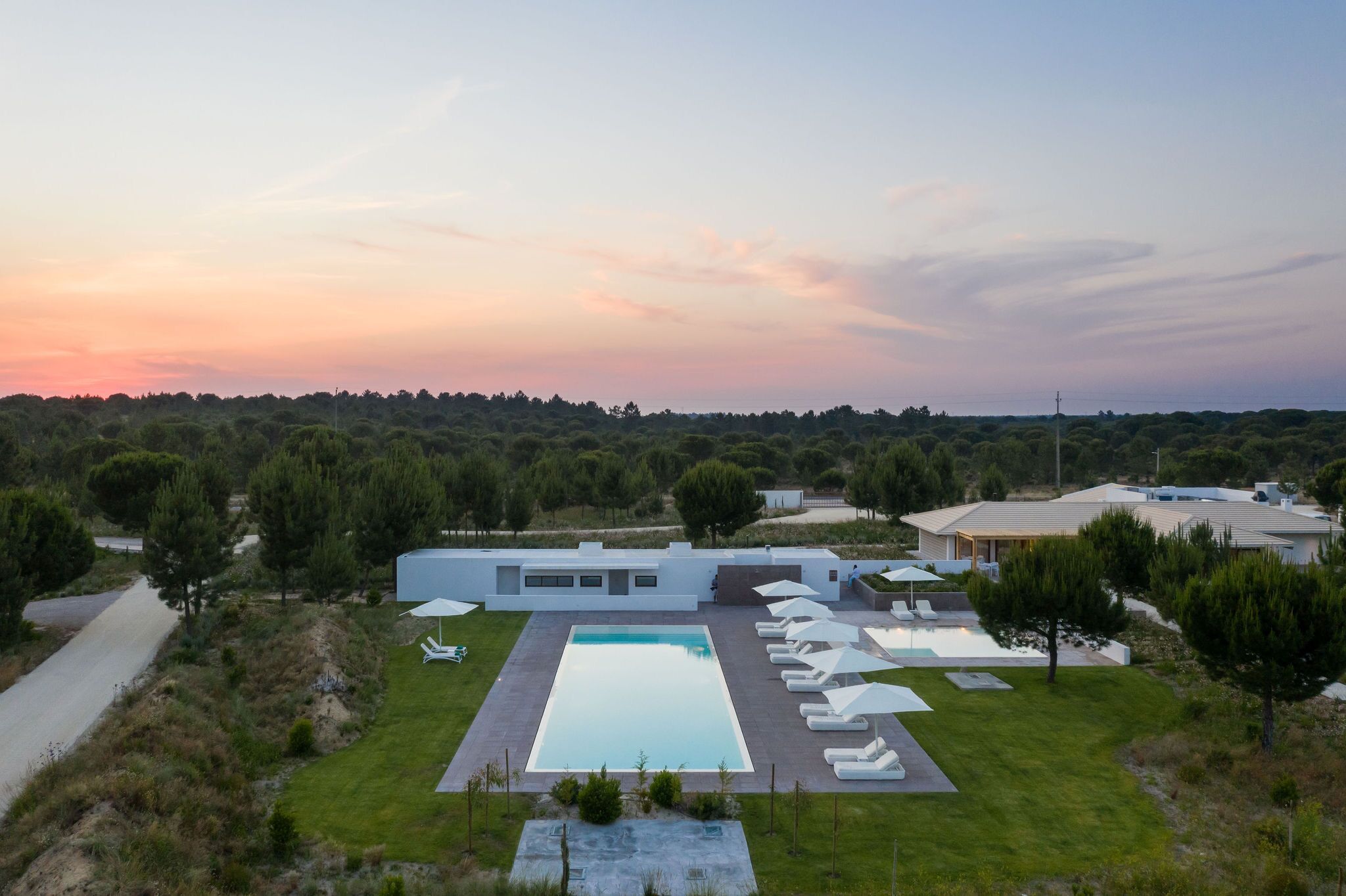 Una casa moderna con piscina, rodeada de césped cuidado y árboles.