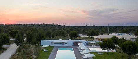 Una casa moderna con piscina, rodeada de césped cuidado y árboles.