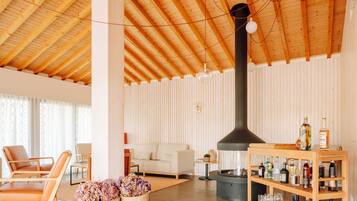 Un vaste espace de vie doté d’un haut plafond en bois, d’une cheminée centrale et d’un bar à boissons en bois.