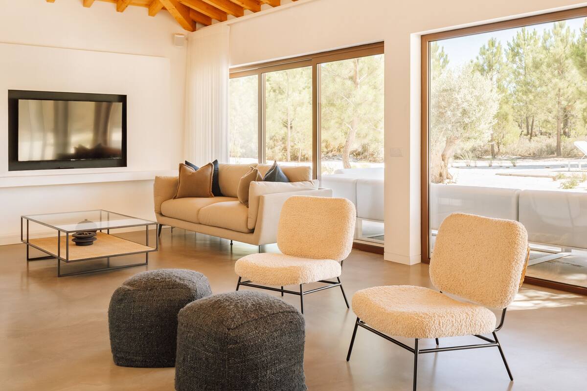 A spacious living room with a high wooden ceiling, large windows, and modern furniture.