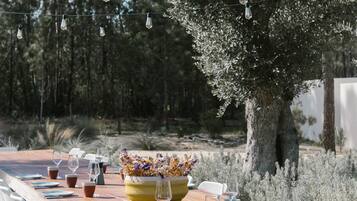 An outdoor dining area with a long wooden table set for a meal, surrounded by chairs.