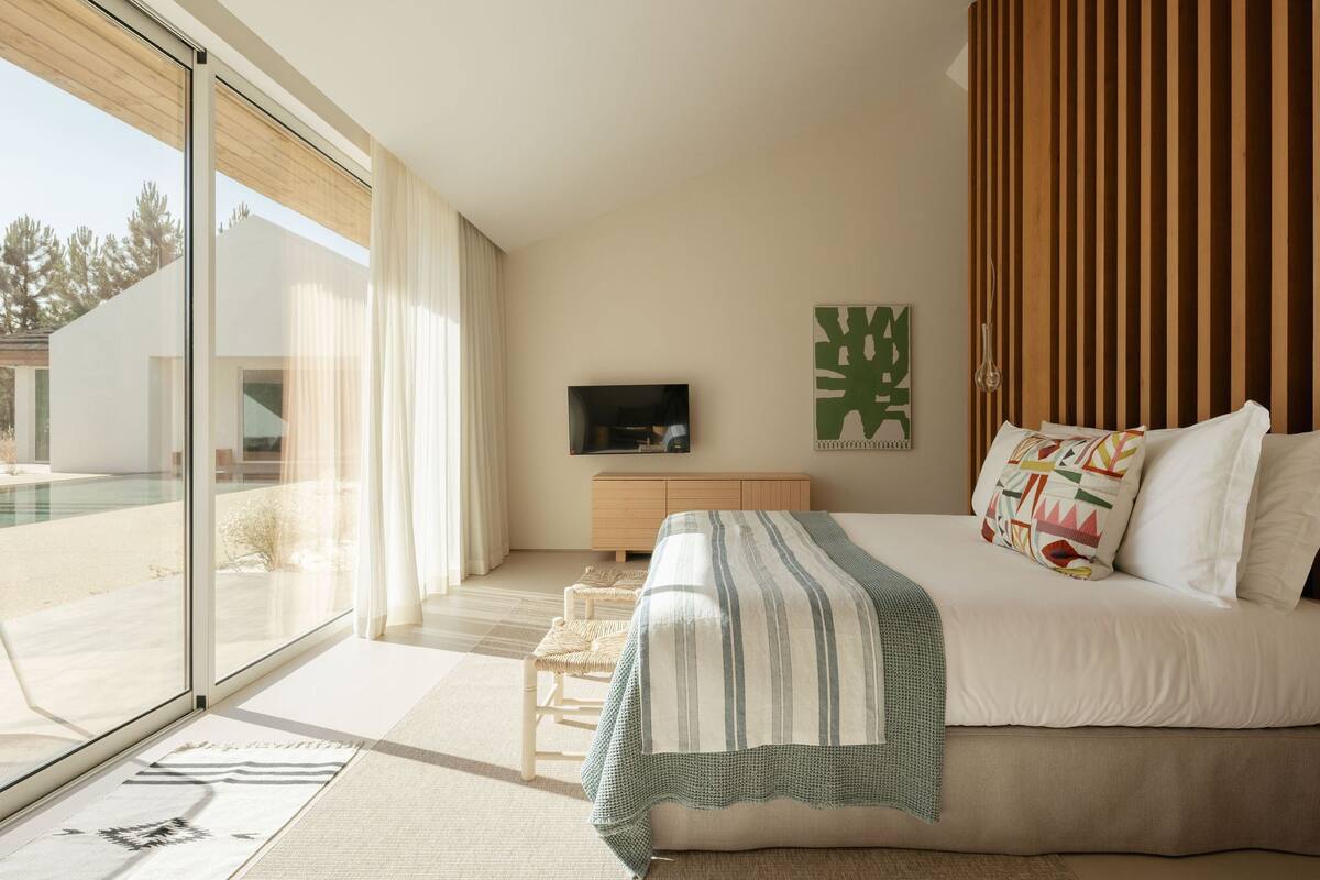 A modern bedroom with a large bed, a television, and a view of a swimming pool.
