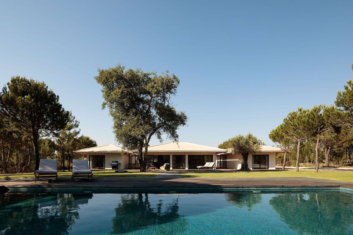 A pool with lounge chairs, a covered patio, and a house with a large tree in front.