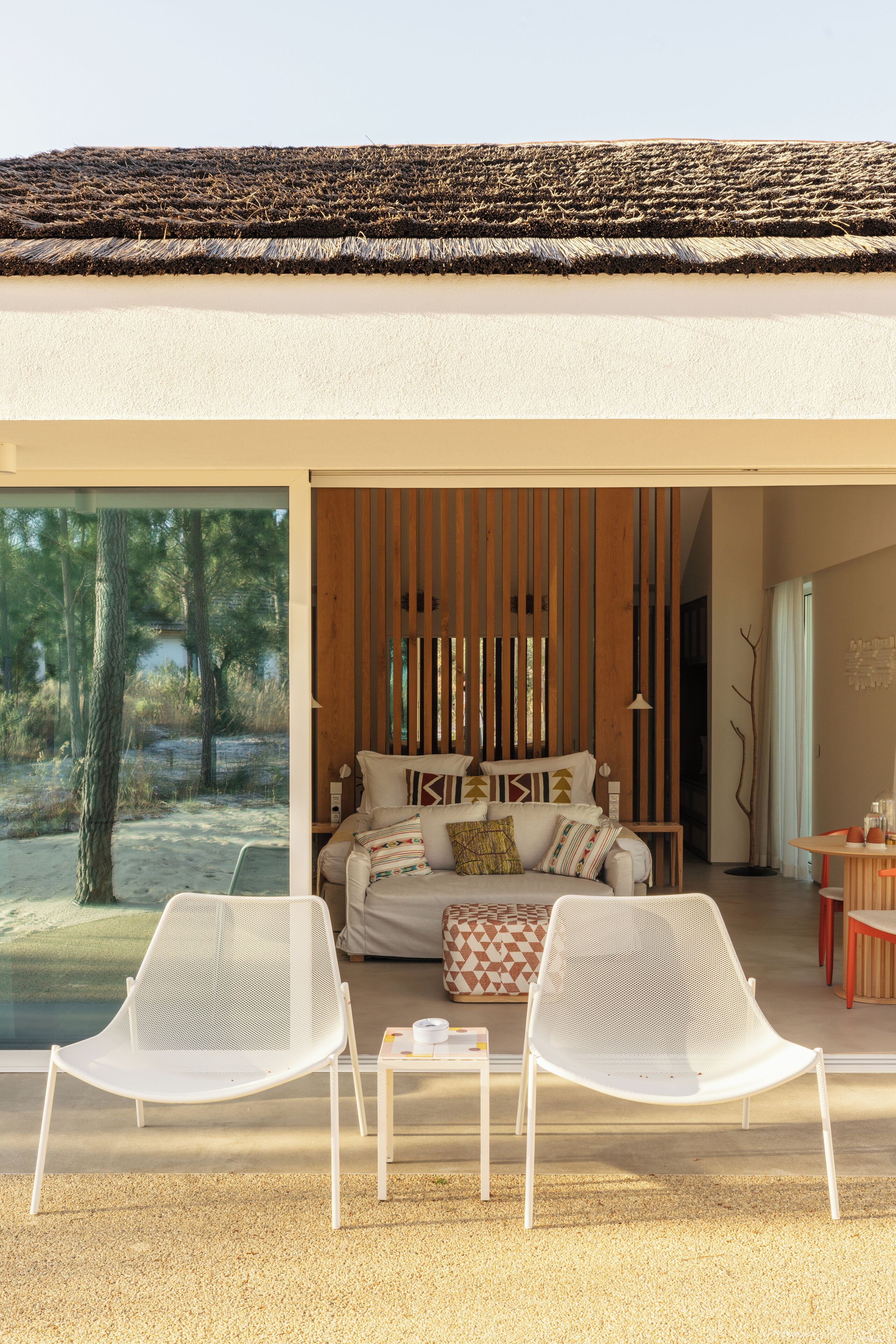 A modern interior with a sofa set, two white chairs, and a view of a natural landscape through large windows.
