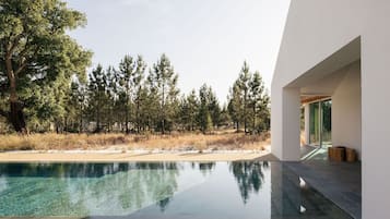 Experience serene views from expansive windows, surrounded by a tranquil pool and lush greenery.