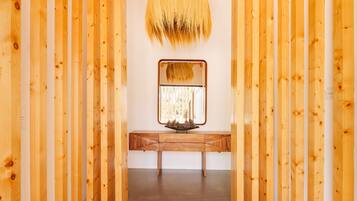 A hallway with wooden walls and a ceiling, leading to a bench with a mirror and a small table with pinecones.