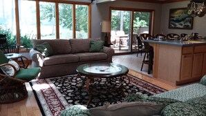Ein geräumiges Wohnzimmer mit braunem Sofa, grünen Sessel, Couchtisch und einer Küchenzeile mit Bar und Essbereich.