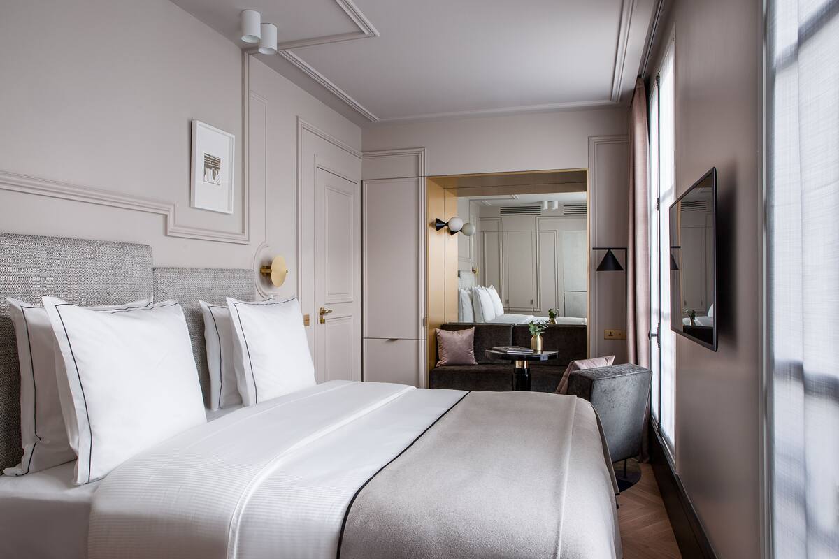 A hotel room with a large bed, a small table, a chair, a mirror, and a window with curtains.