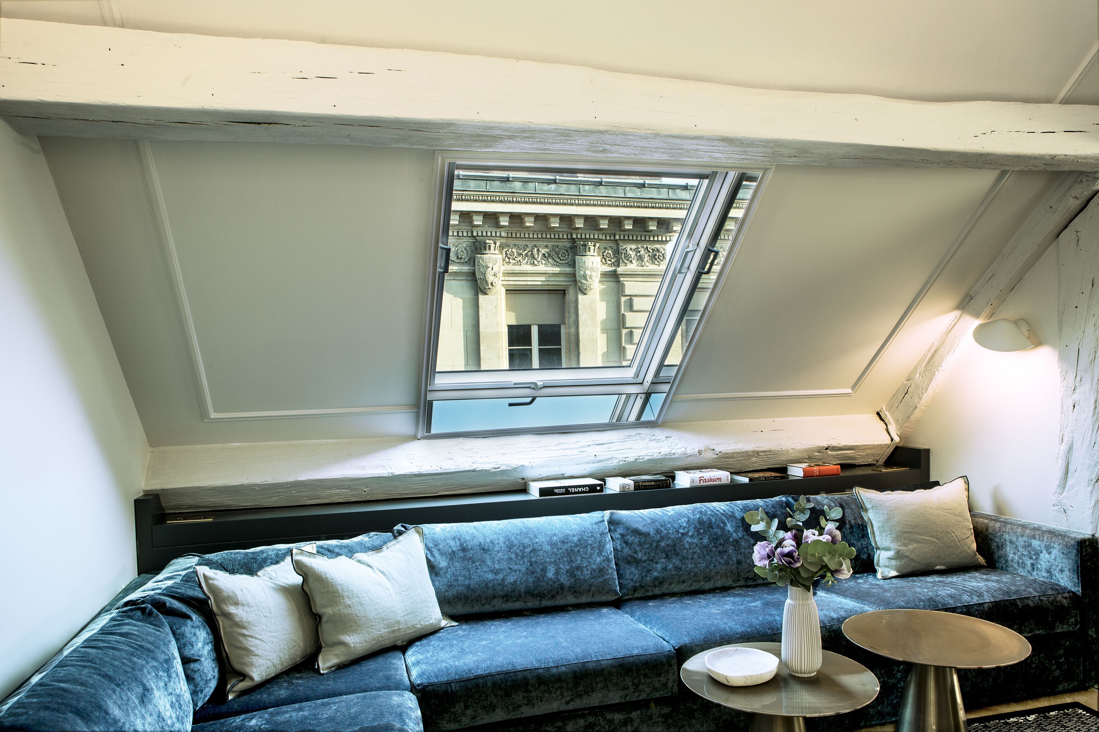Een kamer met een blauwe bank, een klein tafeltje en een raam met uitzicht op klassieke architectuur.