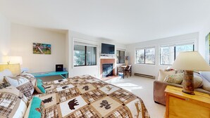 A bedroom with a large bed, a desk, a fireplace, and multiple windows. - Cottonwood Condo 1453B - Walk to Shops, Restaurants & Sun Valley Resort (Sun Valley)