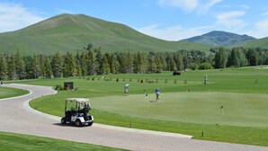 A golf course with a paved driving range, a clubhouse, and a scenic mountainous backdrop. - Cottonwood Condo 1453B - Walk to Shops, Restaurants & Sun Valley Resort (Sun Valley)