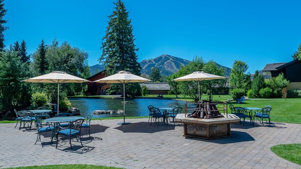 An outdoor patio with tables and chairs, a fire pit, and a view of a mountain and lake. - Cottonwood Condo 1453B - Walk to Shops, Restaurants & Sun Valley Resort (Sun Valley)