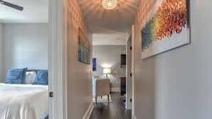 A narrow hallway with a bed on the left, a chair in the center, and a dining area at the end. - Charming Historic King James Building Unit #3 (Asheville)