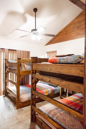 Une chambre avec un lit superposé, un ventilateur de plafond, des murs en bois et une fenêtre avec des stores.