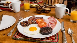 Un plato de desayuno con huevos, salchichas, tomates y jamón.