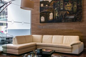 Una sala de estar moderna con un sofá seccional color beige, una mesa de centro negra y un cuadro grande de un edificio histórico en la pared.