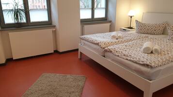 Une chambre à coucher avec un lit, une table de chevet, une lampe, un radiateur et une fenêtre agrémentée d’une plante.