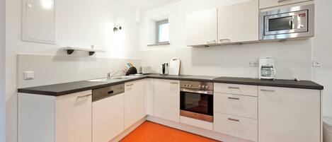 A modern kitchen with white cabinets, a black countertop, and an orange floor.