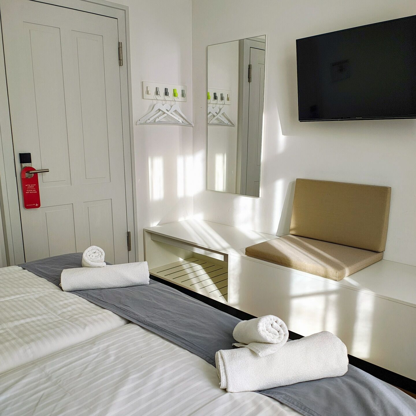 Une chambre d’hôtel avec deux lits, une table de chevet, un miroir, une télévision et un panneau rouge indiquant la sortie de secours.