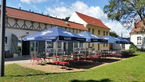 Outdoor seating with umbrellas, tables, and chairs in front of a building with a tiled roof. - Hotel Brandenburger Dom GmbH (Brandenburg an der Havel)