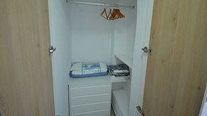A small, white closet with wooden doors, containing a folded white towel, a package of anti-diarrheal medication, and a hanging rack with a few items.